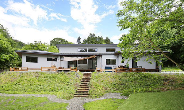 緑に開いた「くの字」の平屋の家