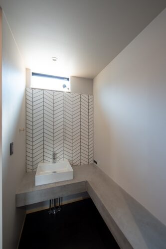 ヘリンボーンのタイルと、モルタルのカウンターがアクセントの洗面室