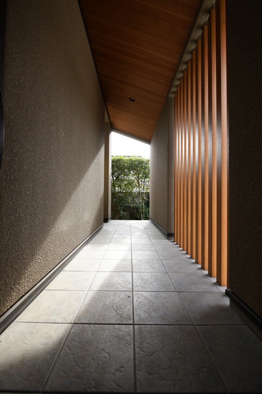 格子から漏れ出す陽光が内部空間へと誘う玄関アプローチ