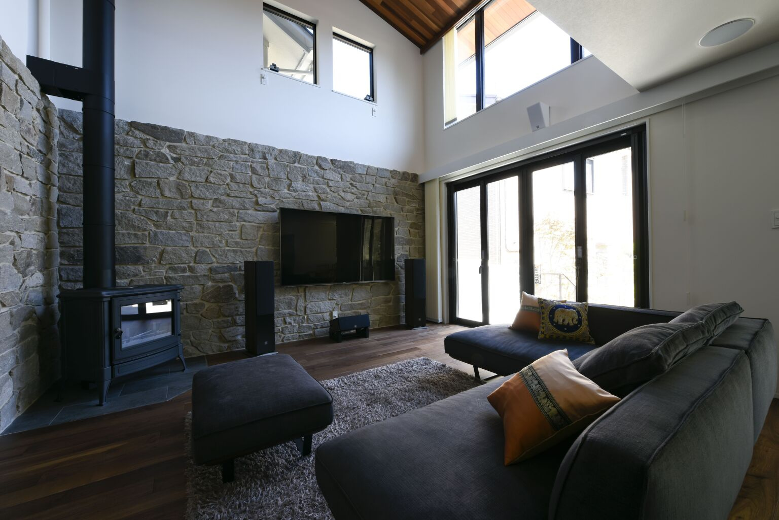 石張りの壁と重厚感のある薪ストーブが映える吹き抜けリビング